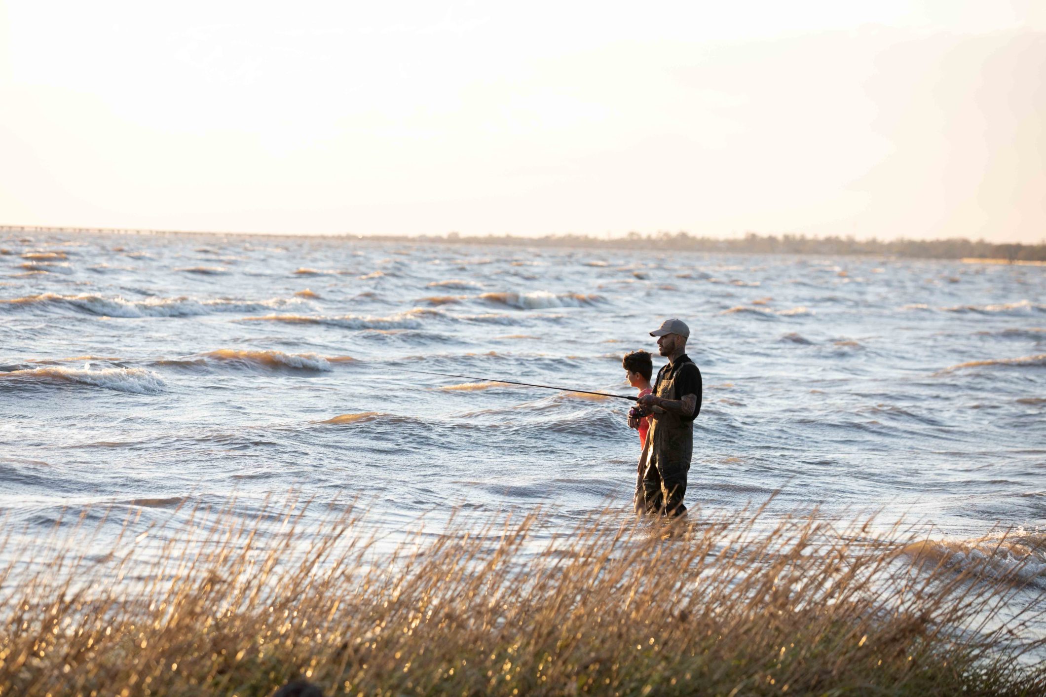 two men fishing standing in water fishing with marsh grass in the foreground