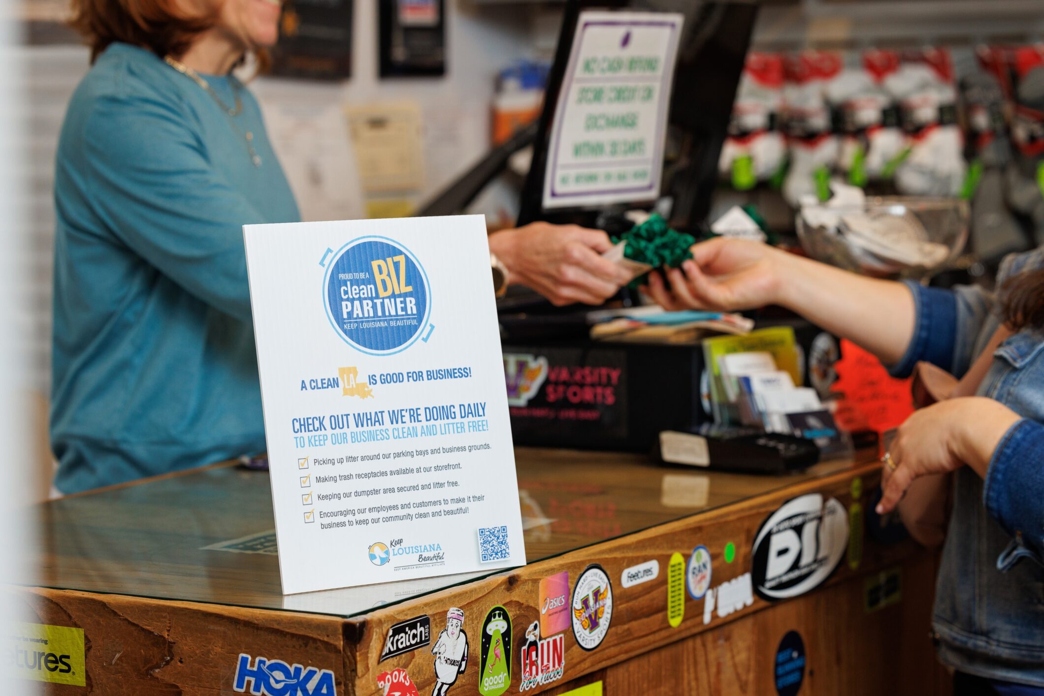 A "Clean Biz Partner" sign displayed on a store counter, listing daily actions taken to keep the business clean and litter-free.