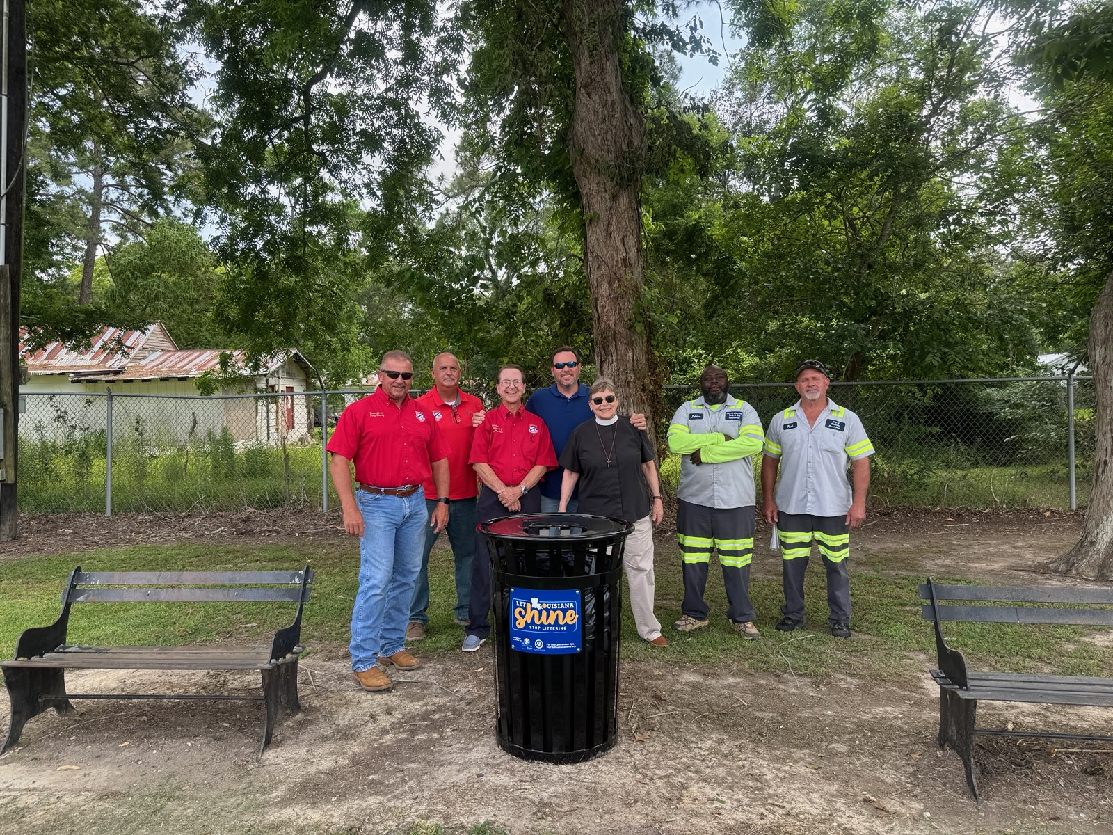 A group of people smiling around a new trash receptacle.