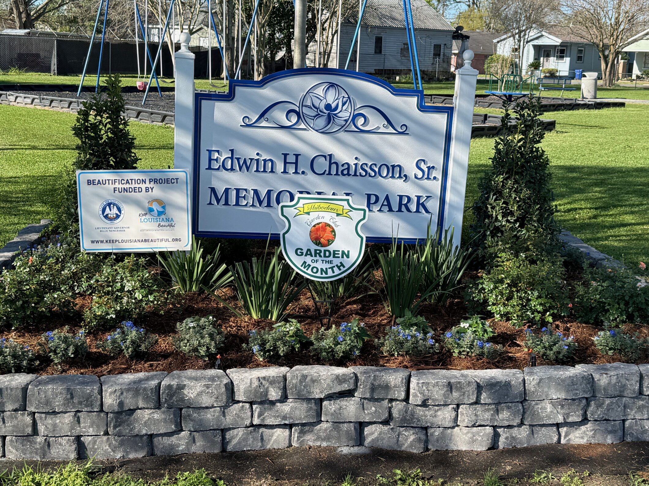 A sign for "Edwin H. Chaisson, Sr. Memorial Park" surrounded by a flower bed with Keep Louisiana Beautiful and Garden Club signs.