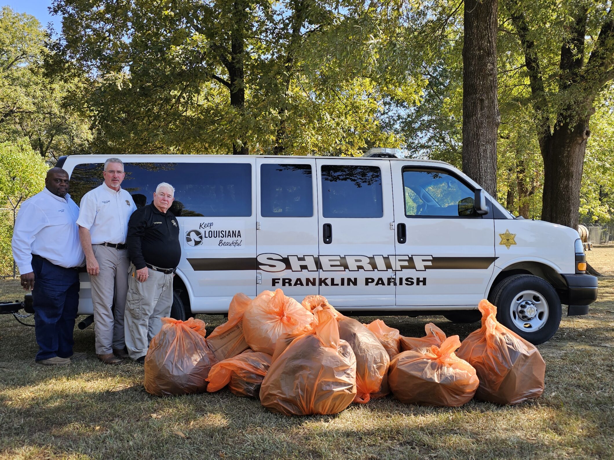 Men standing around a sheriff van with bags full of collected trash.