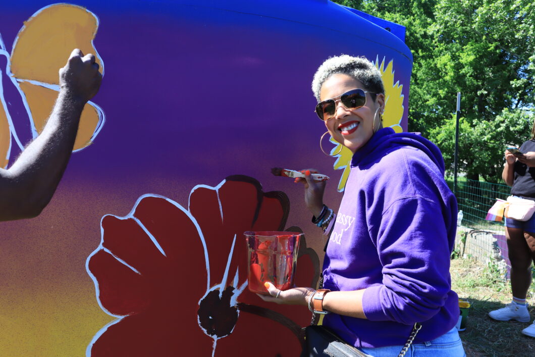 A volunteer smiling while painting a large flower as part of the new cistern mural.
