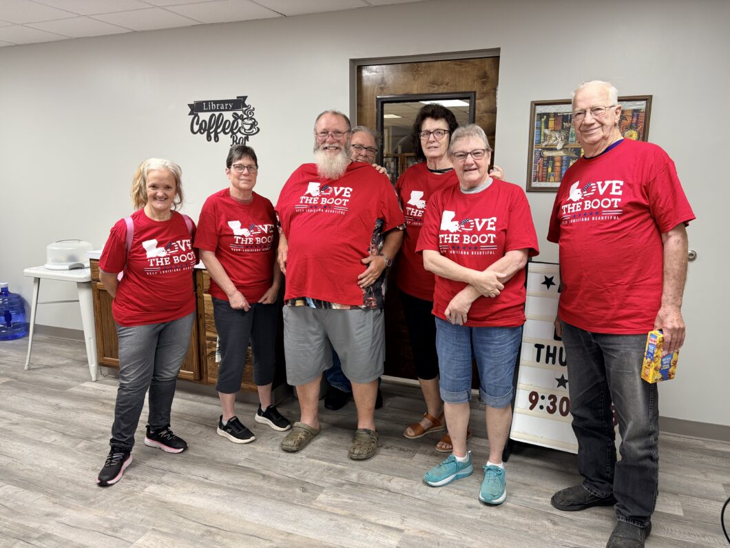 A group of volunteers wearing red Love the Boot Week shirts stand together inside the Evangeline Parish Library during a community cleanup event.