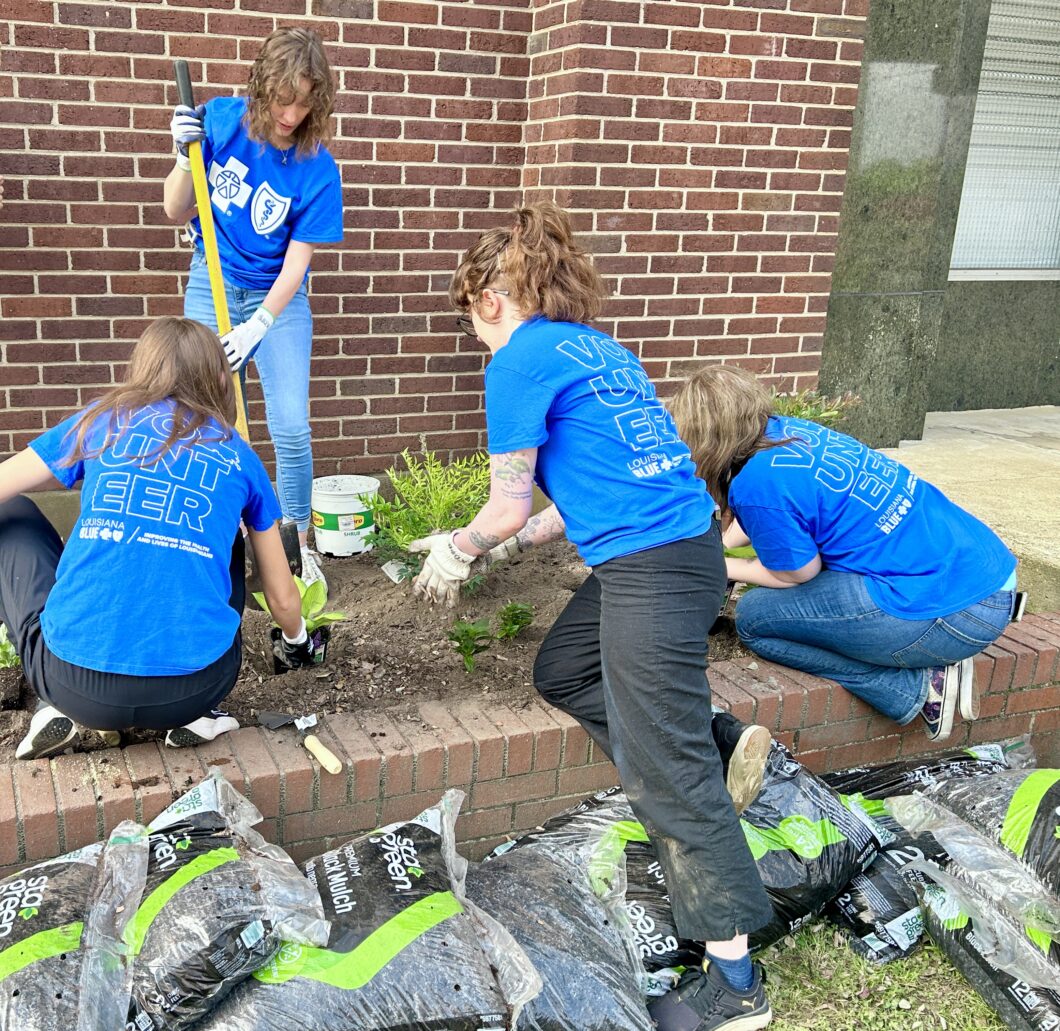 Four Louisiana Blue volunteers planting garden plants and flowers in a bed.