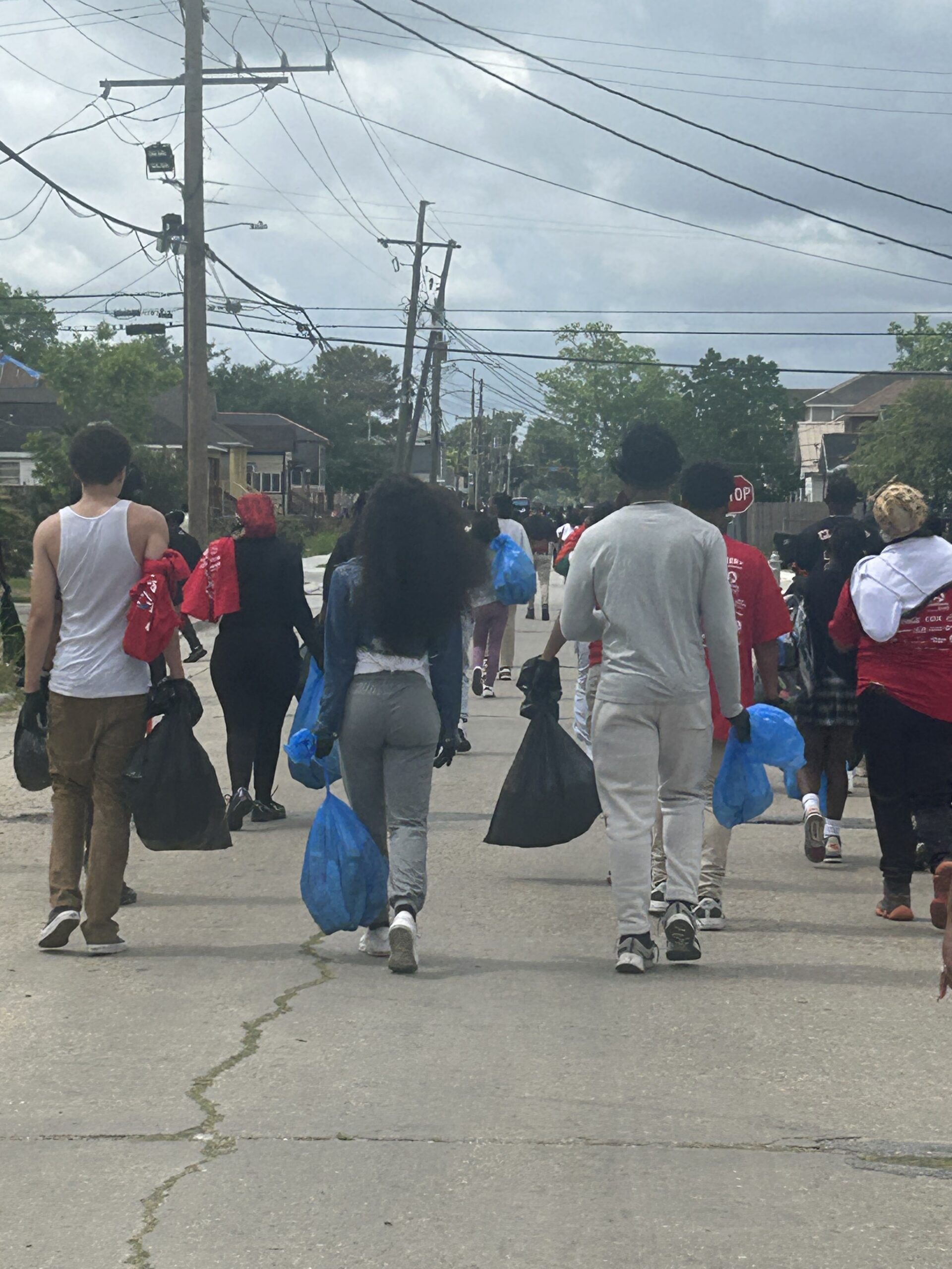 Students and volunteers from G.W. Carver High School walk through a neighborhood carrying trash bags and cleanup supplies during a Love the Boot Week litter cleanup event.