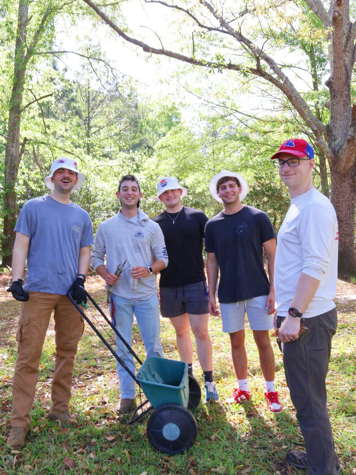 Five Louisiana Tech University Student Government Association students stand outdoors during a Love the Boot Week cleanup event. The group poses with cleanup tools and a small cart in a wooded area while volunteering to remove litter and beautify their community.