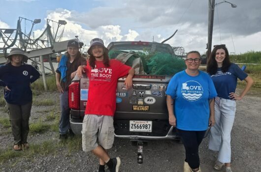 Five volunteers pose beside a truck loaded with nets and cleanup supplies during a Love Our Waterways event